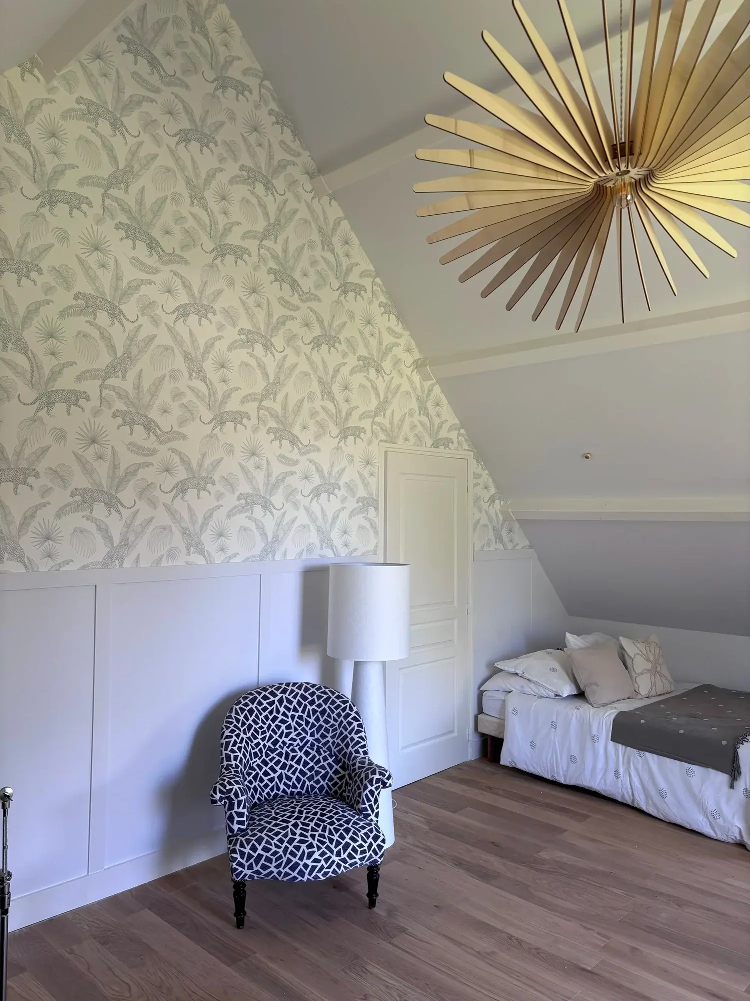 Pièce sous les toits, papier peint végétal, fauteuil à motifs et suspension dorée