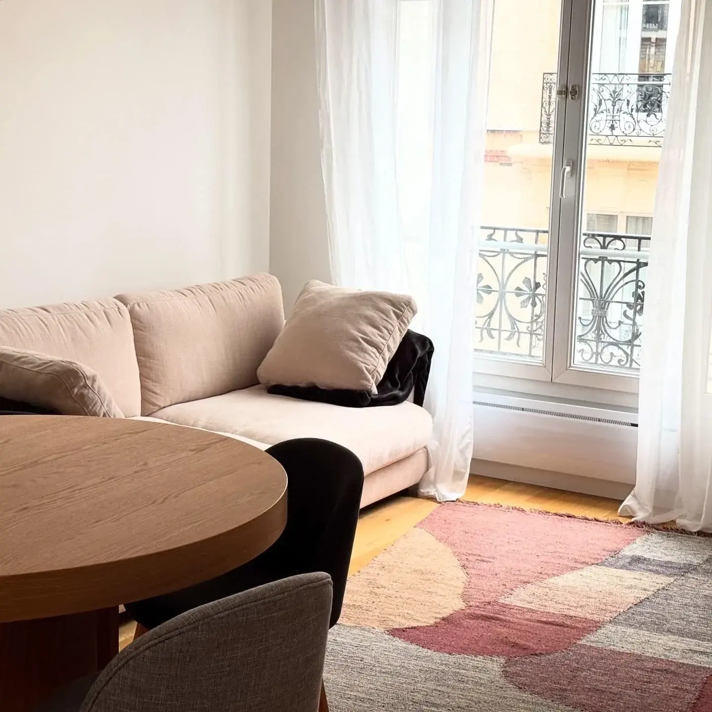 Séjour lumineux avec canapé beige, table ronde en bois et tapis aux formes douces