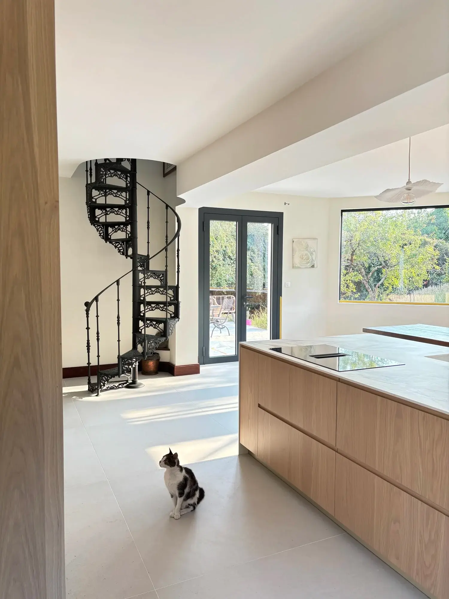 Vue d’ensemble de la cuisine, escalier en colimaçon et grandes baies vitrées