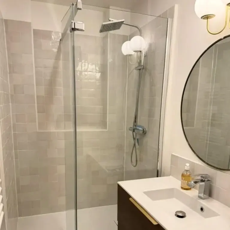 Salle d’eau en zellige clair, miroir rond et douche à l’italienne