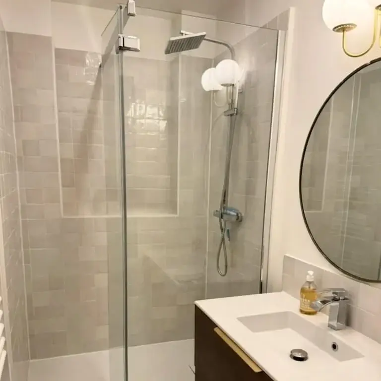 Salle d’eau en zellige clair, miroir rond et douche à l’italienne