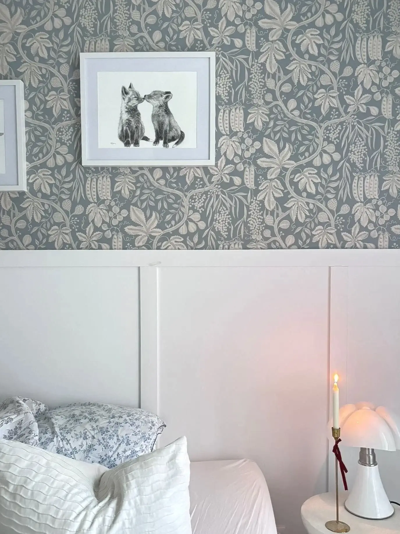 Chambre parentale : papier peint botanique bleu, soubassement blanc, cadre aux lapins et bougie allumée