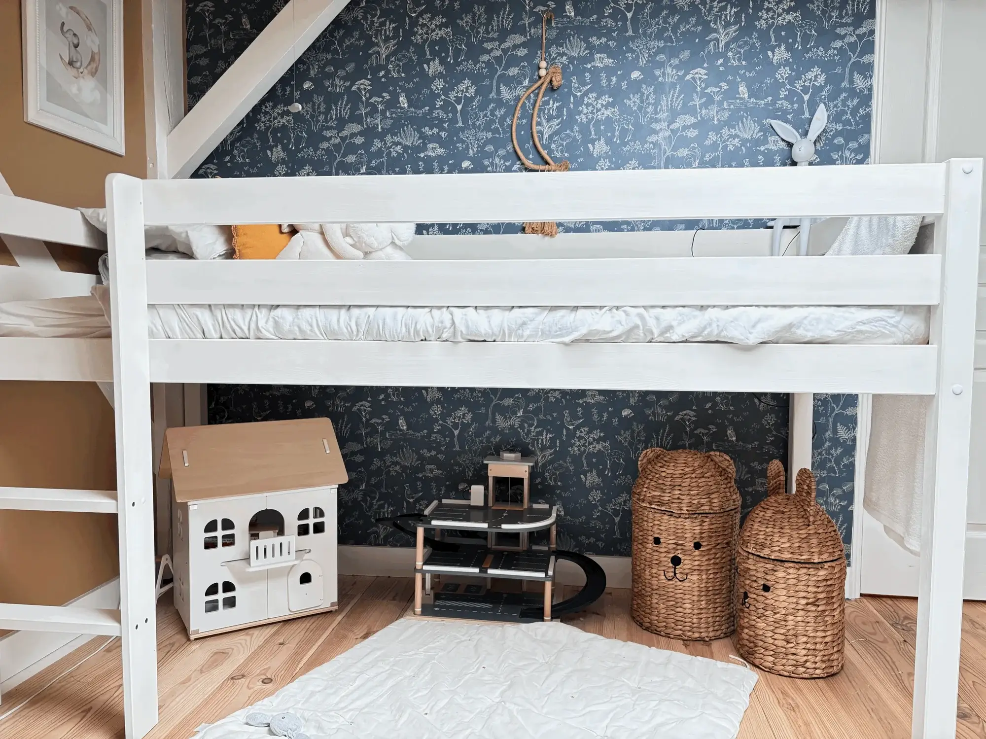 Chambre d’enfant avec lit mezzanine blanc, papier peint botanique bleu nuit et paniers tressés